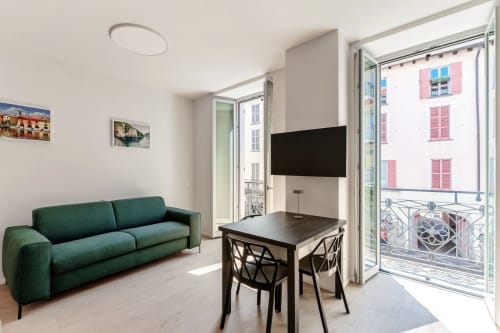 Salotto moderno a Lago Suites Como con divano verde, TV a schermo piatto, tavolo da pranzo e balcone con vista sulla città