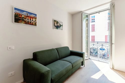 Divano verde moderno nella camera d'hotel Como con vista città dal balcone e opere d'arte incorniciate su muri bianchi