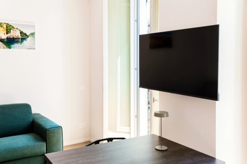 Camera moderna del Lago Suites Como con TV a parete, poltrona turchese e balcone con vista sulla città
