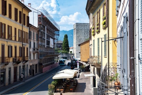 Vista storica della strada di Como da Lago Suites con edifici gialli, montagne e sedute in terrazza all'aperto