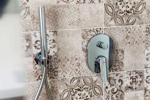 Moderni rubinetti cromati in doccia su parete decorativa con piastrelle beige nella suite del Lago Suites Como