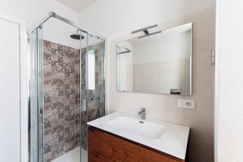 Bagno moderno di Lago Suites Como con doccia in vetro, mobile con lavabo in legno e specchio a parete