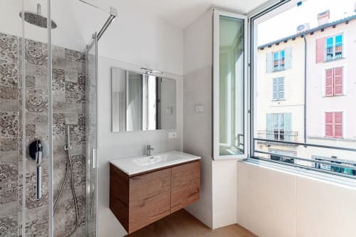 Moderno bagno di Lago Suites Como con vanity in legno, piastrelle decorate, doccia a pioggia e vista sulla città dalla finestra