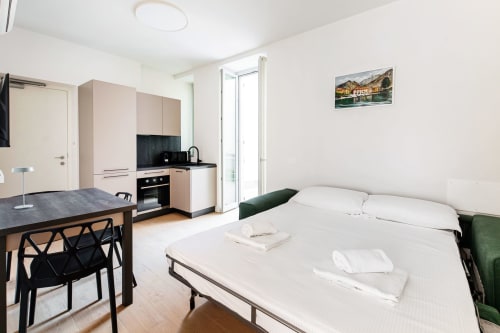 Studio moderno presso Lago Suites Como con letto, angolo cottura, zona pranzo e poster con vista sulla città