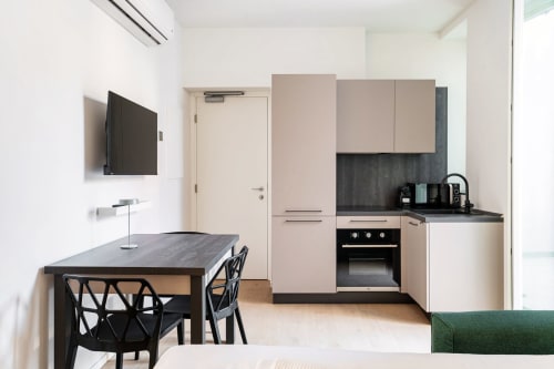 Moderna cucina con zona pranzo nella Room 102 di Lago Suites Como, con tavolo nero, TV a parete e spazi compatti