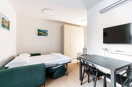 Camera moderna di Lago Suites Como con letto, divano verde, scrivania, TV e vista sulla città