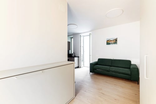 Suite open-plan moderna presso Lago Suites Como con divano verde, zona cucina e balcone con vista sulla città