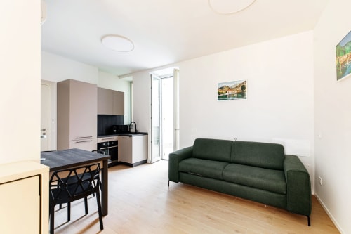 Moderno appartamento a Lago Suites Como con divano verde, cucina, tavolo da pranzo e vista sulla città