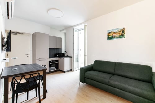 Camera 102 Lago Suites a Como: monolocale moderno con divano verde, tavolo da pranzo, angolo cottura e vista sulla città