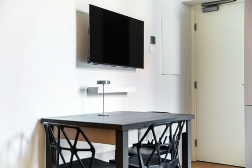 Spazio di lavoro moderno presso Lago Suites Como con TV a parete, scrivania con sedie nere e porta color crema