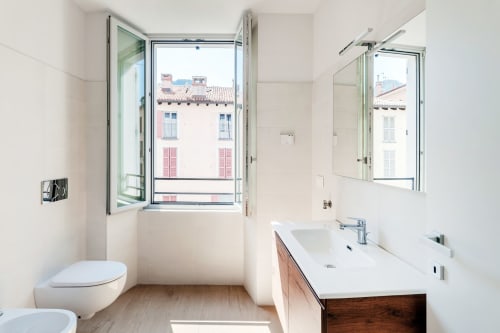 Bagno moderno di Lago Suites Como con doppio lavabo e vista sulla città attraverso finestre che si affacciano su architettura storica