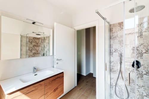 Bagno moderno di Lago Suites Como con vanity in legno, lavabo bianco, specchio e doccia con piastrelle decorative