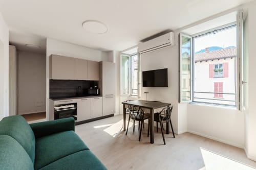 Studio moderno presso Lago Suites Como con cucina, zona pranzo, divano verde, TV e balcone con vista sulla città