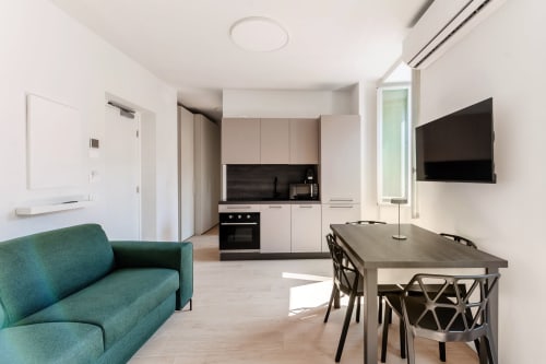 Camera 201 moderna al Lago Suites Como con divano teal, tavolo da pranzo, angolo cottura, TV a parete e vista sulla città