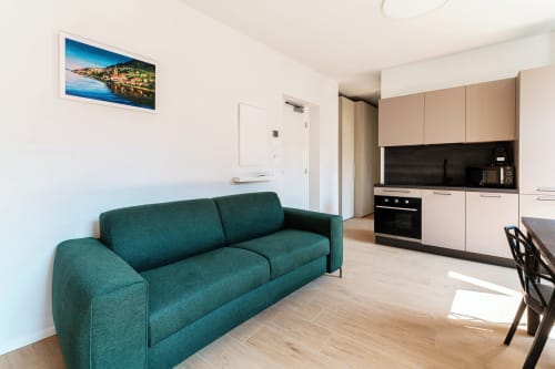 Cucina a pianta aperta e zona living moderna presso Lago Suites Como con divano teal e opere d'arte con vista sulla città