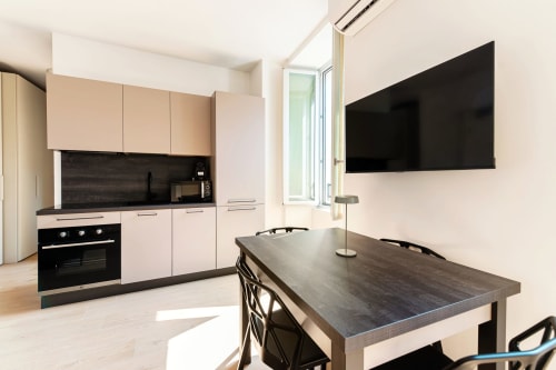 Cucina e zona pranzo moderna presso Lago Suites Como con TV a parete, forno nero, mobili chiari e tavolo da pranzo scuro