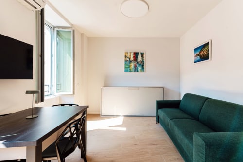 Camera moderna di Lago Suites Como con scrivania scura, divano turchese, TV, letto a scomparsa e vista sulla città