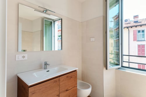 Moderno bagno di Lago Suites Como con vanità in legno, specchio e finestra con vista sull'architettura urbana
