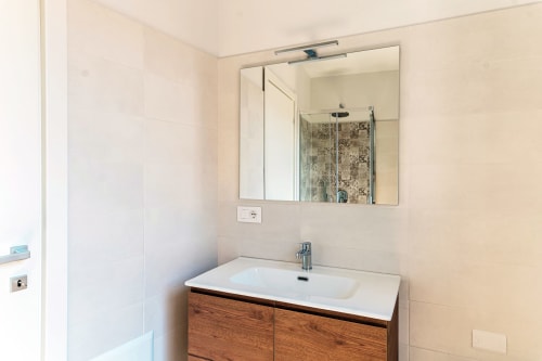 Bagno moderno di Lago Suites Como con vanity in legno, lavabo in marmo bianco e ampio specchio con applique