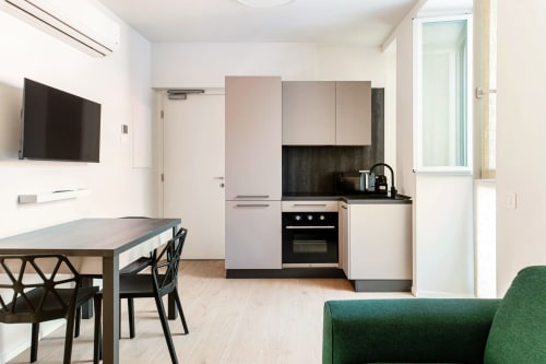 Camera moderna di Lago Suites Como con angolo cottura, tavolo da pranzo, TV e poltrona verde