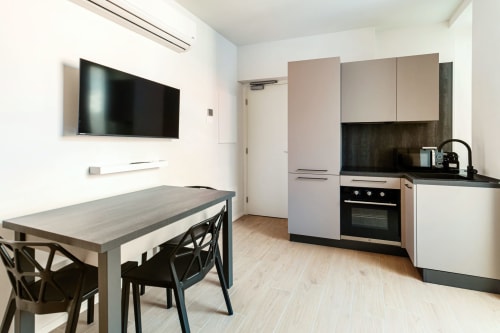 Cucina e zona pranzo moderne nella Camera 202 di Lago Suites Como, con TV a parete, tavolo da pranzo con sedie nere e