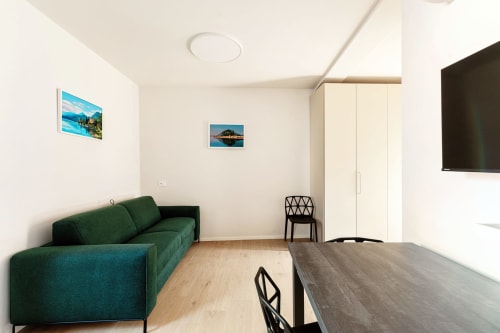 Camera moderna presso Lago Suites Como con divano verde, tavolo da pranzo, TV e vista panoramica sul lago