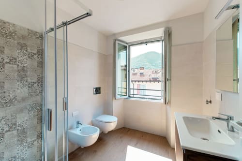 Bagno moderno di Lago Suites Como con doccia, bidet, wc, lavabo e vista sulla città dalla finestra
