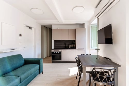 Monolocale moderno presso Lago Suites Como con divano turchese, tavolo da pranzo, cucina e TV a parete