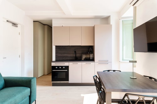 Moderna camera studio presso Lago Suites Como con cucina, tavolo da pranzo, poltrona turchese e TV a schermo piatto