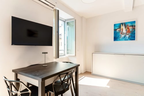 Camera moderna presso Lago Suites Como con scrivania scura, TV a parete, quadro di barca a vela e finestra aperta sulla città