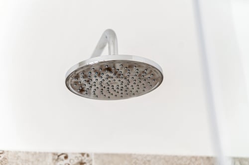 Soffione doccia cromato montato su parete bianca del bagno presso Lago Suites Como