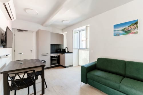 Moderna zona cucina-living a Lago Suites Como con divano verde, tavolo da pranzo e vista sulla città