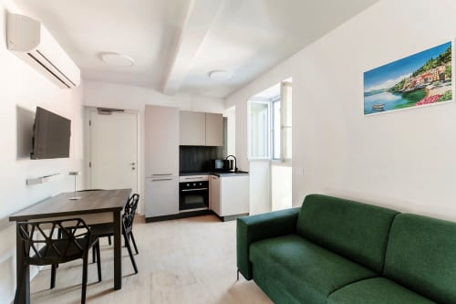 Moderno monolocale a Como con divano verde, angolo cottura, zona pranzo e vista sulla città presso Lago Suites