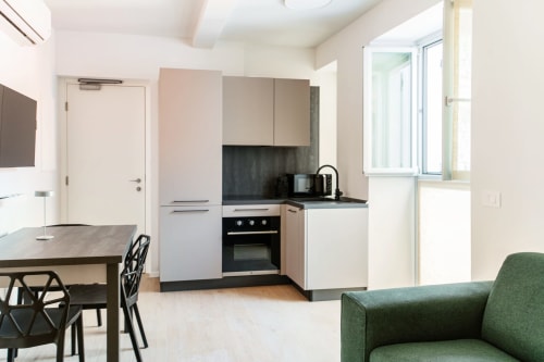 Moderna cucina e zona living nella Suite 302 di Lago Suites Como con mobili bianchi, piano nero, tavolo da pranzo e verde