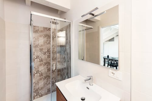 Bagno moderno presso Lago Suites Como con doccia in vetro, vanità bianca, specchio e design neutro in ceramica