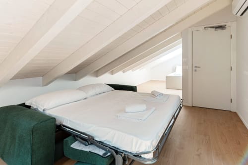 Camera da letto mansardata minimalista presso Lago Suites Como con travi a vista, biancheria bianca e pavimenti in legno