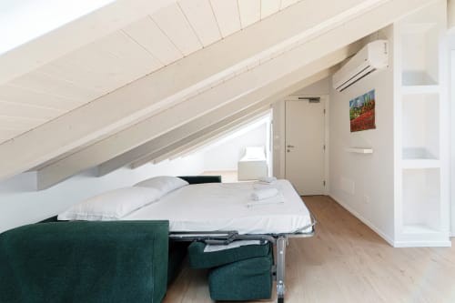 Camera da letto mansardata di Lago Suites Como con soffitto spiovente, biancheria bianca, divano verde e vista sulla città