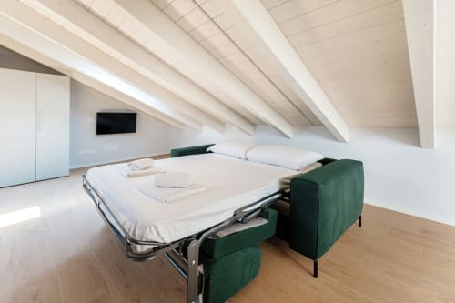 Camera da letto moderna in mansarda a Lago Suites Como con letto a scomparsa, poltroncine verdi, parquet e travi a vista