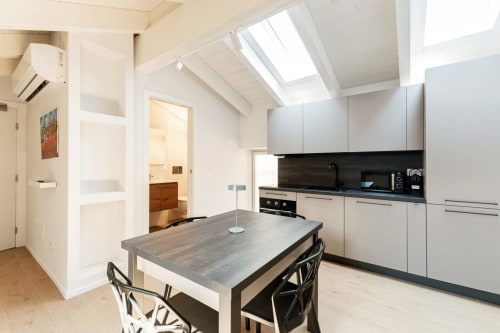 Cucina moderna presso Lago Suites Como con tavolo da pranzo, mobili bianchi, rivestimento nero e lucernario