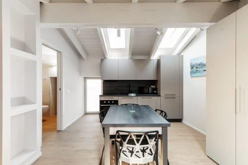 Cucina-soggiorno moderna presso Lago Suites Como con lucernario, boiserie grigia, tavolo isola e vista città su pareti bianche