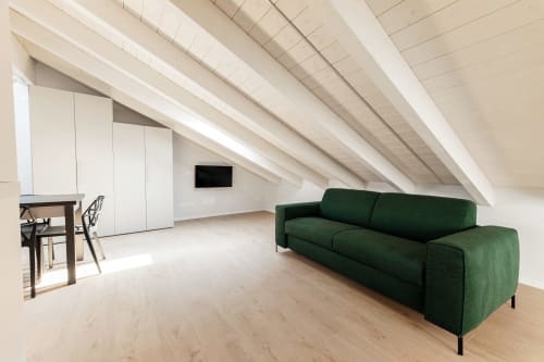 Moderna camera mansardata a Lago Suites Como con divano verde, ripostiglio bianco integrato, scrivania in legno e TV flat-screen