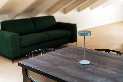Moderna camera d'albergo a Como presso Lago Suites con tavolo in legno scuro, lampada blu e divano verde sotto travi a vista