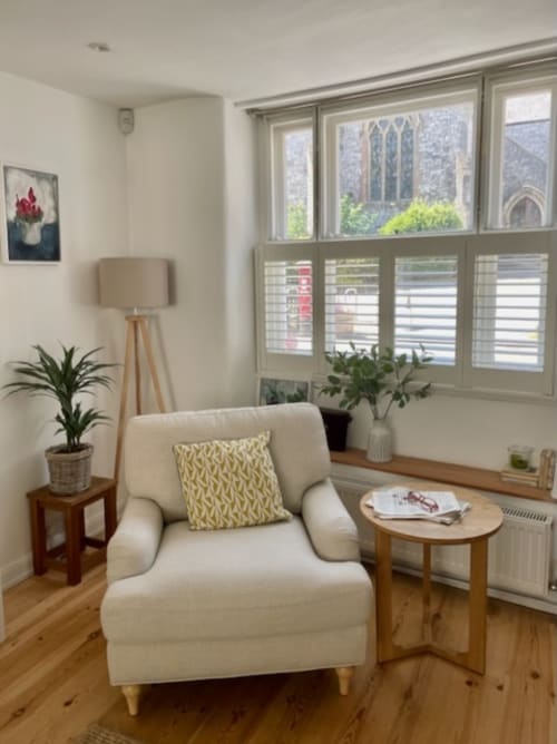 Bright sitting area at 2 Doves Holiday Property in Exeter with cream armchair, wooden side table, potted plants, and large