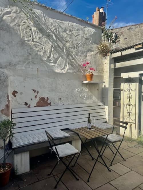 Cozy outdoor garden patio at 2 Doves Holiday Property in Topsham, Exeter, featuring bench seating, dining table, and pink