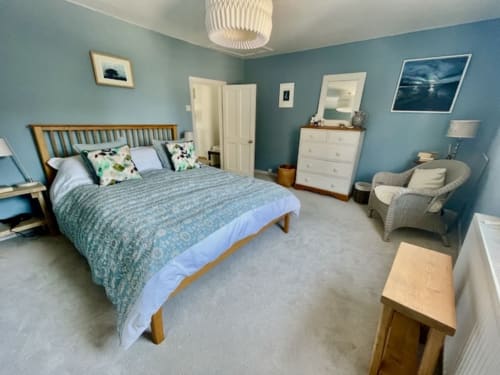 Bright blue bedroom at 2 Doves Holiday Property in Exeter with wooden bed, white dresser, armchair, and coastal artwork