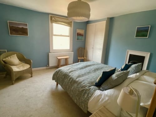 Spacious bedroom at 2 Doves Holiday Property in Exeter with turquoise walls, double bed, wicker chair, window, wardrobe and