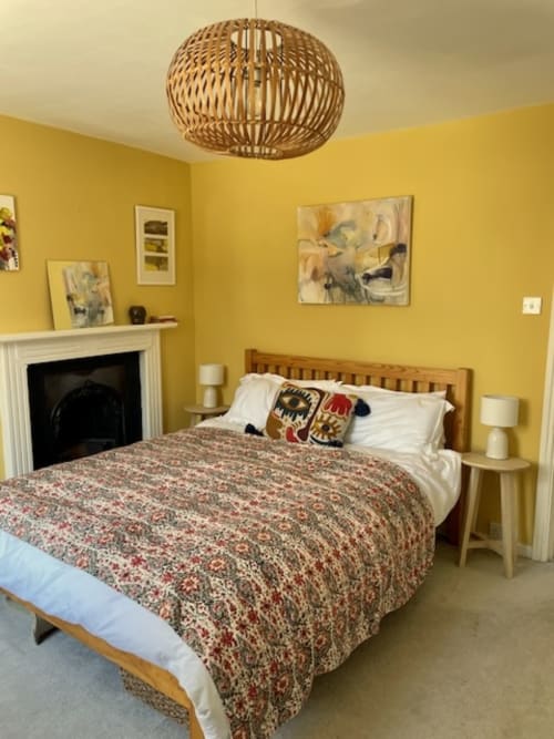 Bright yellow bedroom at 2 Doves Holiday Property in Topsham with wooden bed, fireplace, woven pendant light, and framed