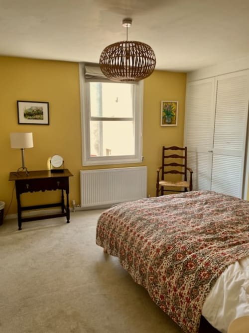 Bright yellow bedroom at 2 Doves Holiday Property in Exeter with bed, desk, wooden chair, woven pendant light, and city views