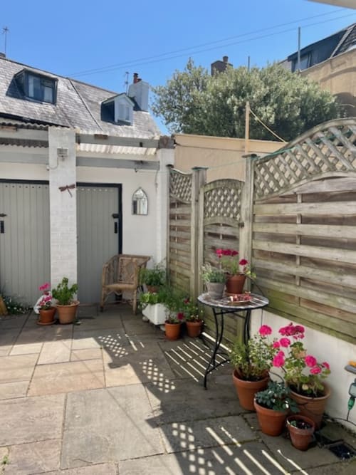 Private patio garden at 2 Doves Holiday Property in Topsham with pink flowers, wooden furniture, and lattice fencing
