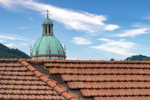 Chiesa con cupola di rame verde affacciata sugli antichi tetti di terracotta nel panorama di Como, Italia